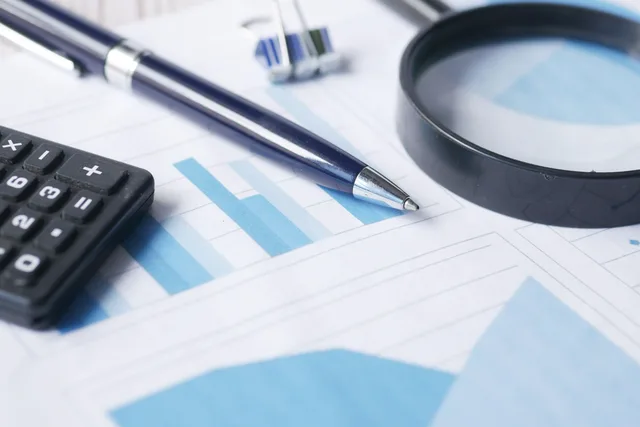 Close-up of calculator, pen, and magnifying glass on financial documents. Commercial insurance premium audit: what happens after the policy year ends
