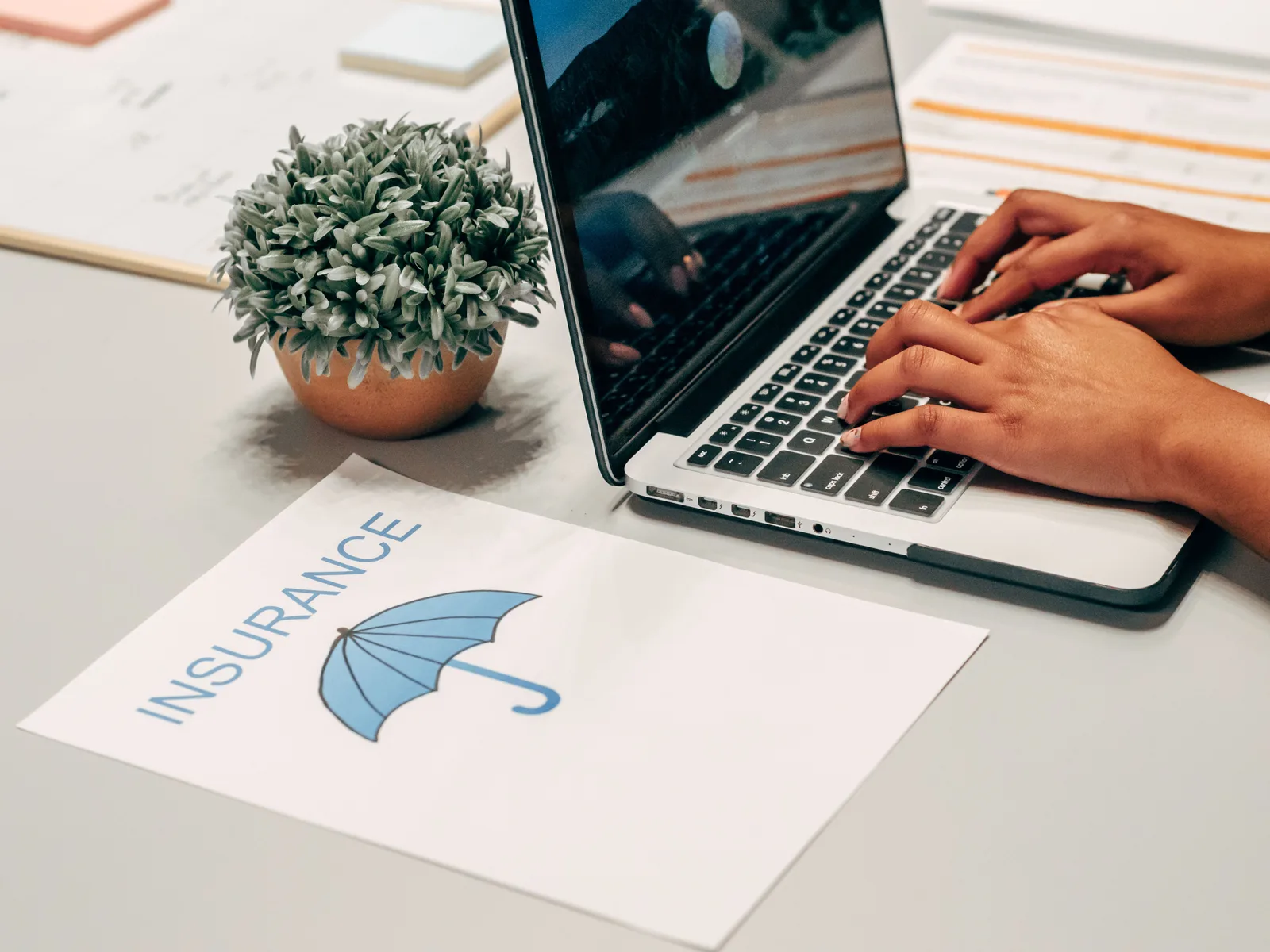 Hands typing on a laptop at a desk with an insurance paper and plant, suggesting a work environment. Commercial insurance premiums after a claim: what changes and when
