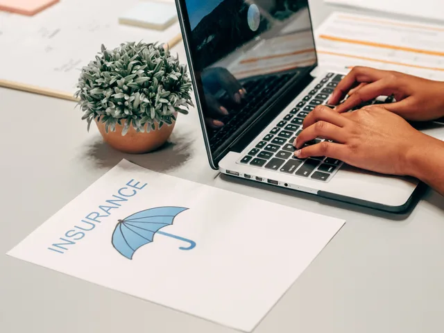 Hands typing on a laptop at a desk with an insurance paper and plant, suggesting a work environment. Commercial insurance premiums after a claim: what changes and when