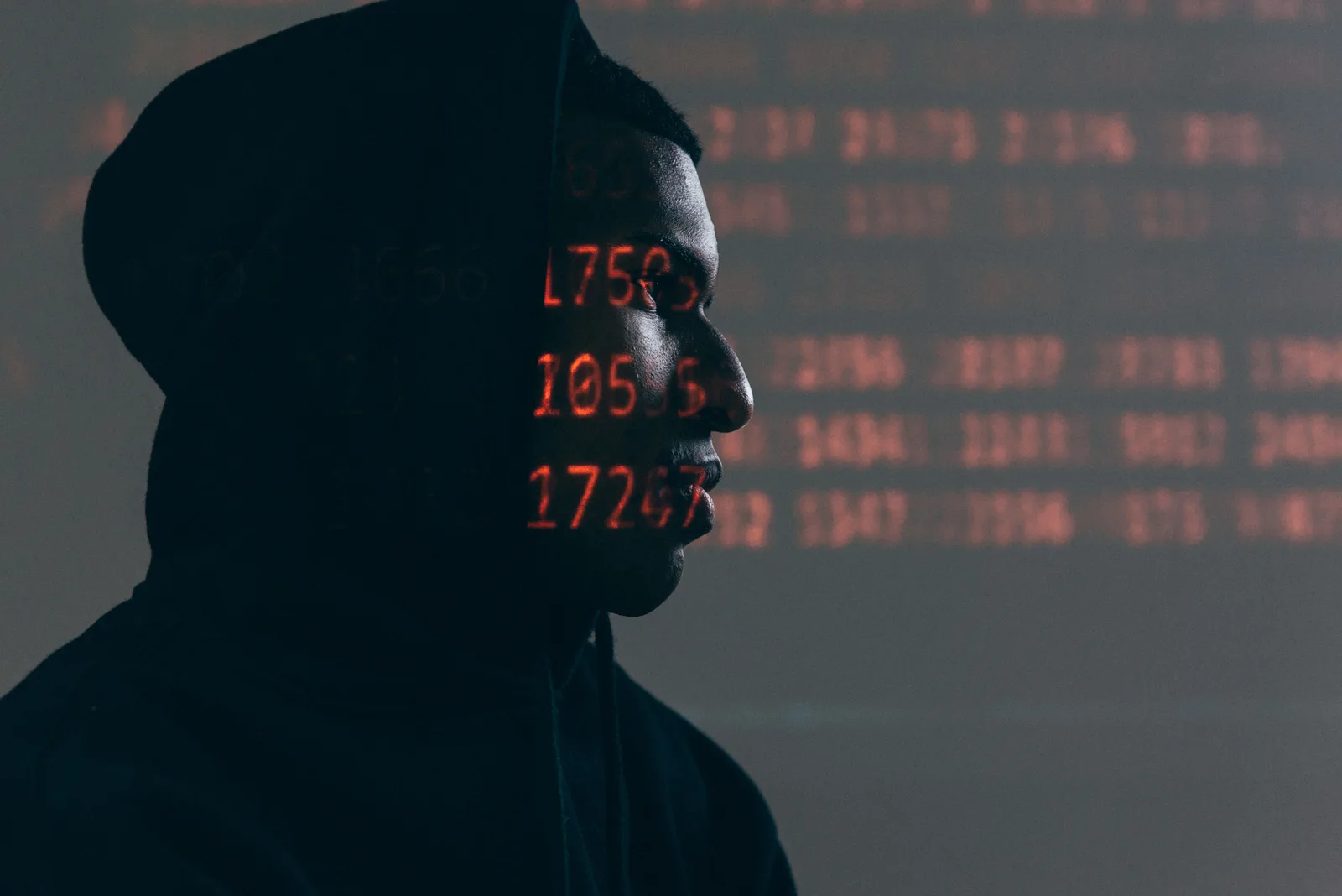 Side profile of a man in a hoodie, surrounded by red code, depicting cybersecurity theme. Cyber insurance examples with the reasoning laid bare