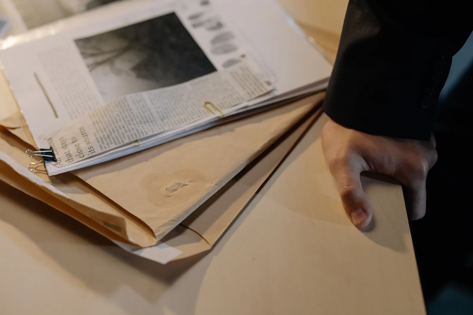 Close-up of a hand resting on a desk near a stack of investigative documents and newspaper clippings. Employee Theft Coverage Limits: How Per-Loss Limits Work