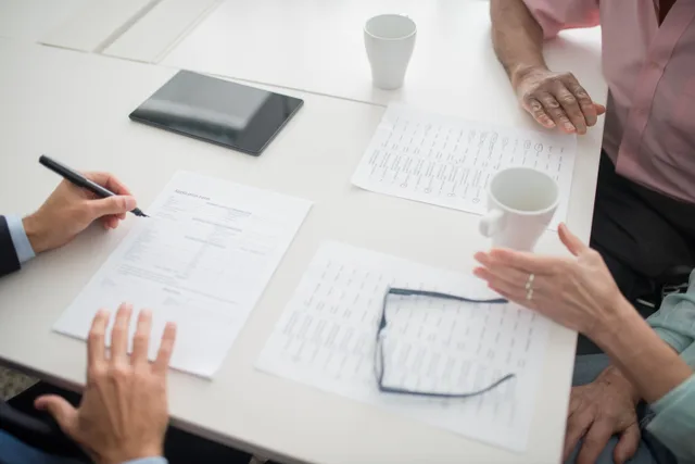 Hands writing on documents in a business meeting setup with coffee cups and tablet. Handling a general liability review, offer, or disputed claim in three steps