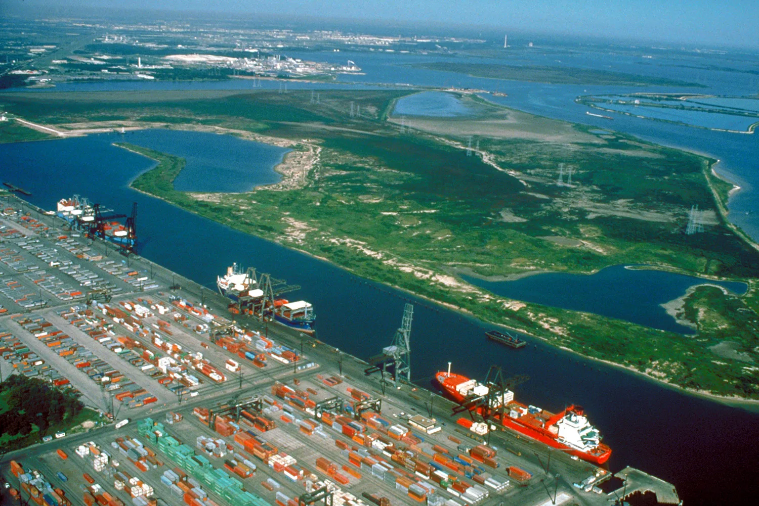 Aerial view of the Barbour's Cut area on the Houston Ship Channel in Houston, Texas, USA. This area is a large container terminal. This photograph appears to have been taken before the Fred Hartman Bridge was built, or when the bridge was under construction. In a present-day photograph, the bridge s. Houston energy and maritime industries, and their specialized commercial coverage needs